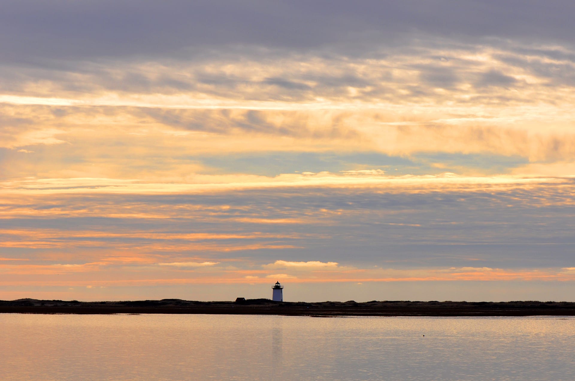 Cape Cod lighthouse at sunset reflecting golden light over calm waters
